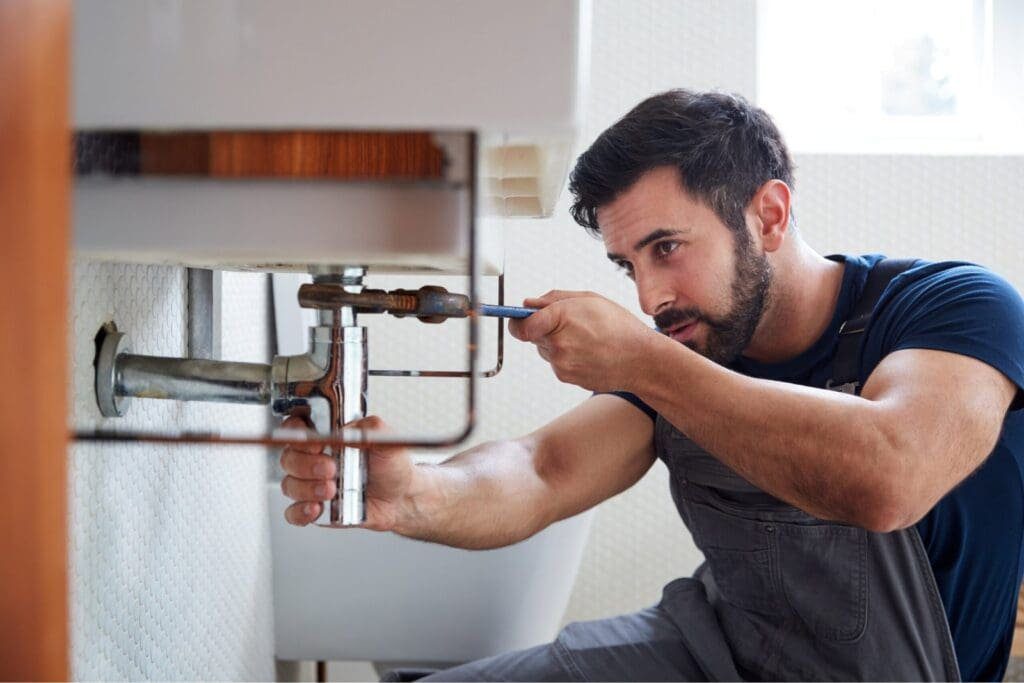 Professional plumber working on sink pipe connections in a bathroom setting.