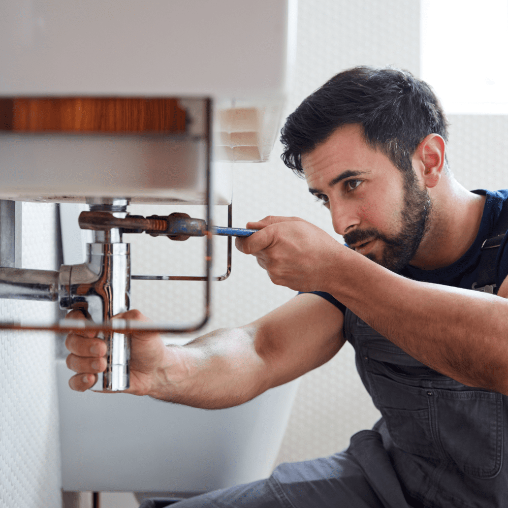 A male plumber using a wrench on pipework under a bathroom sink.